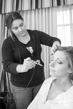 makeup artist applying airbrush makeup to a bride